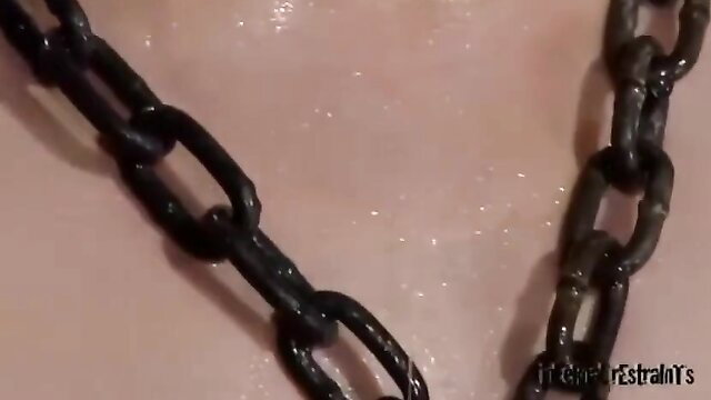 Shiny chains draped on wet pale skin in intense BDSM whipping scene