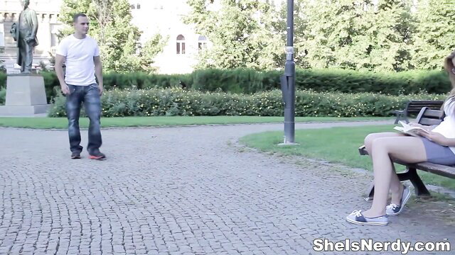 Nerdy girl in glasses and skirt sits on park bench, guy approaches