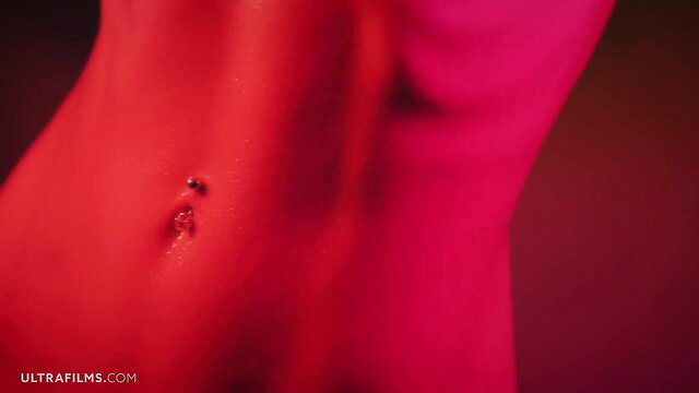 Closeup of woman's sexy red-lit belly with navel piercing