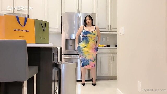 Curvy Latina brunette in tie-dye dress poses in kitchen