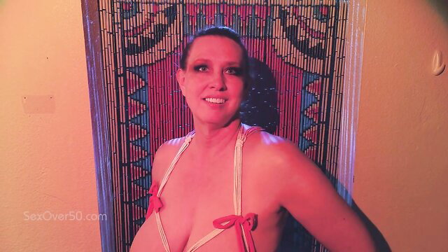 Mature woman in sexy lingerie poses seductively by beaded curtain