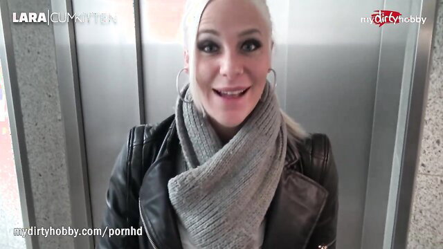Lara Cumkitten blonde in leather jacket scarf smiling in elevator