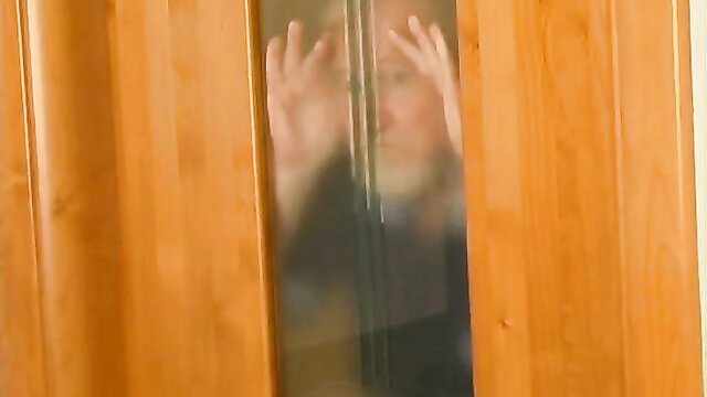 Mature woman pressing hands on glass door in steamy bathroom tease