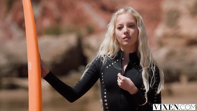 Blonde Kelly Collins in wetsuit holds surfboard on beach VIXEN