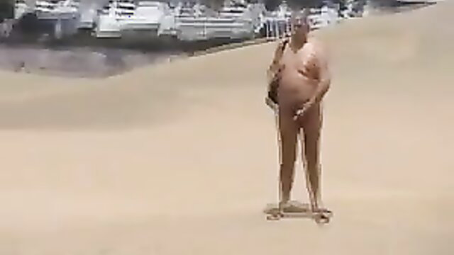 Nude older man skateboarding on sandy beach near water