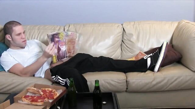 Bald white guy in sweats reading hentai mag on couch with pizza beer