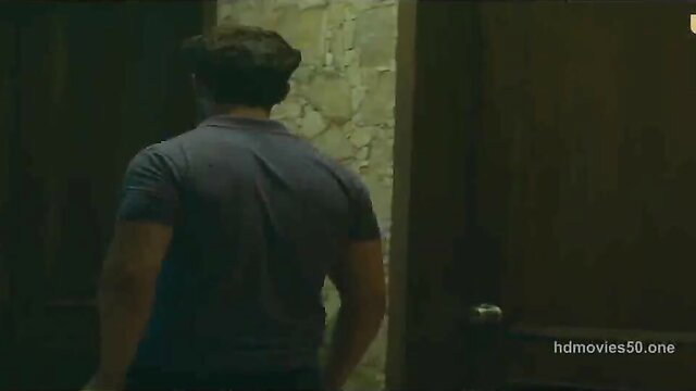 Indian man in grey tank top stands at door in dimly lit room