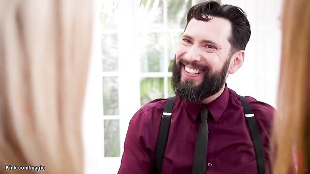 Bearded man in suspenders smiles at camera in sunny room