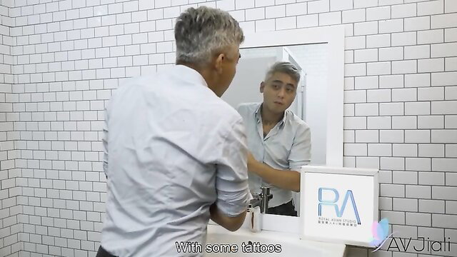 Gray-haired Asian man with tattoos admires himself in mirror