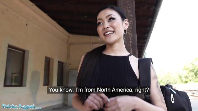 Rae Lil Black Asian beauty smiling on outdoor platform in black dress