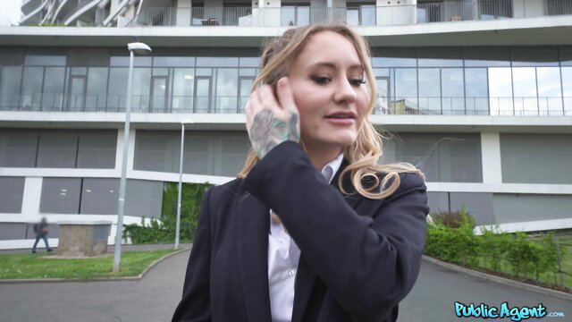 Blonde Ivy Maddox in suit, tattooed hand to ear outside building