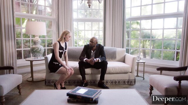 Blonde in black dress kneels for suited black man on couch in Deeper Green Earrings