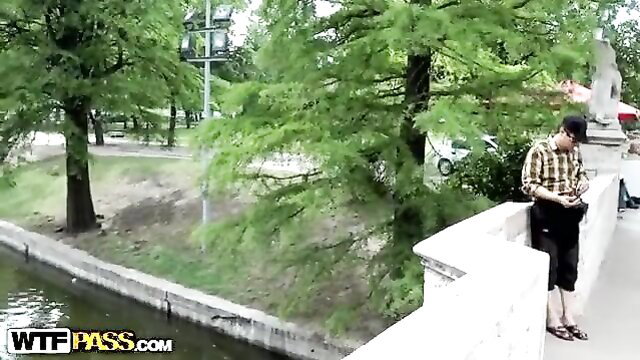 Man in checkered shirt stands by river bridge in park woods