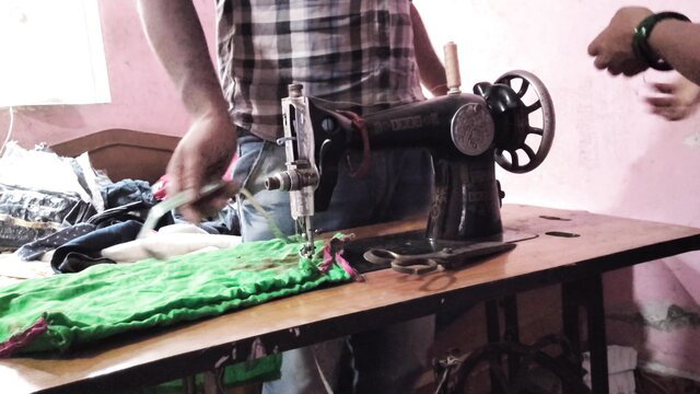 Tailor man sewing green fabric on vintage machine in workshop