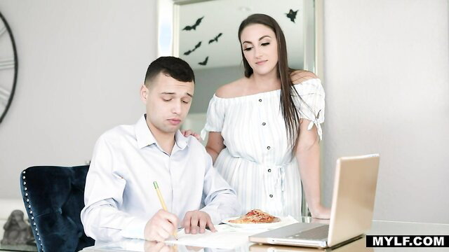 Melanie Hicks in white off-shoulder dress stands over stepson at desk