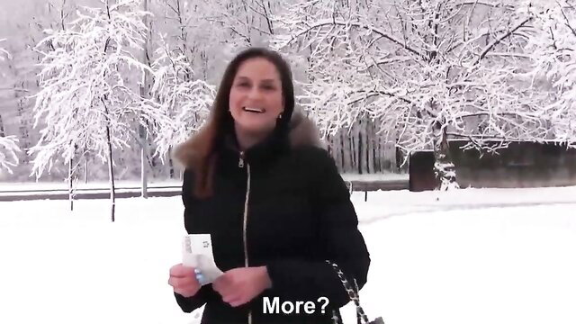 Smiling brunette MILF in black puffer jacket holding box in snowy outdoors