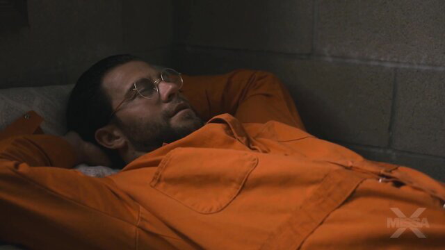 Prisoner man in orange jumpsuit lying on bunk in jail cell