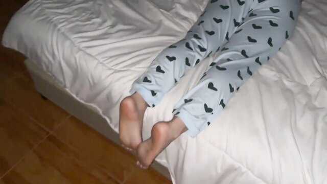 Barefoot teen in heart pajamas lying on bed POV