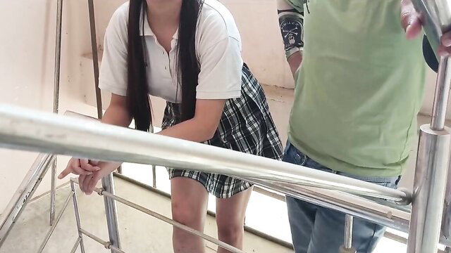 Asian schoolgirl in plaid skirt bends over stair railing with guy