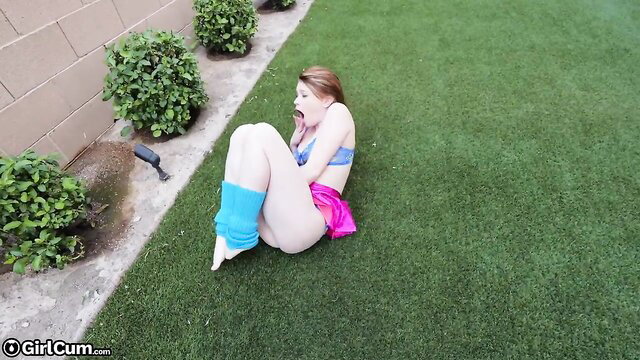 Redhead in leg warmers & skirt on grass, mouth open in pleasure