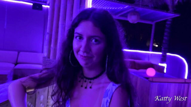 Katty West smiling in neon-lit club, low-cut top, big hoops
