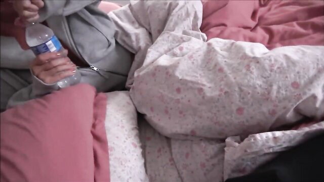 Brianna Beach in grey hoodie on pink bed holding water bottle