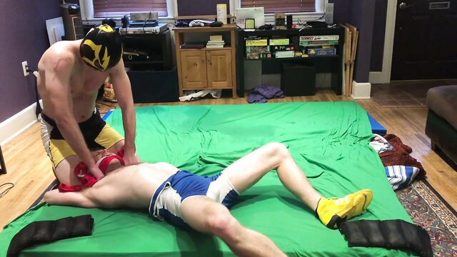 Muscular wrestler in mask dominates shirtless loser in speedo on mat post-match