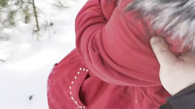 Chubby babe in red parka with fur hood in snowy woods, hand on head