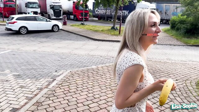 Lisa Sophie blonde in white dress holding banana outdoors by trucks