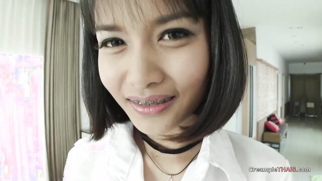 Beautiful petite Thai babe with bangs and braces smiling in white shirt