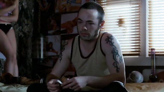 Bald tattooed guy rolling joint with hot babe in lingerie nearby