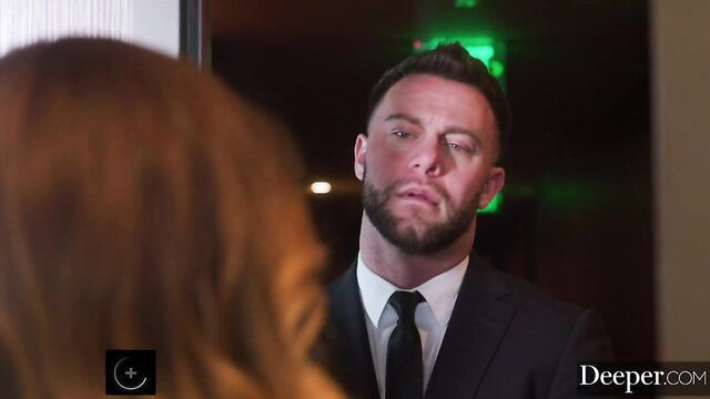 Busty redhead dominatrix in suit teases suited man in mirror reflection