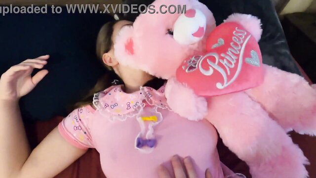 Petite stepdaughter in pink princess onesie cuddles teddy bear