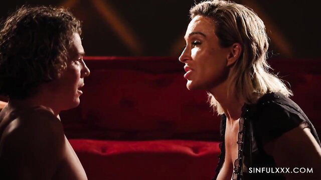 Blonde woman in lingerie seduces young curly-haired man on red couch