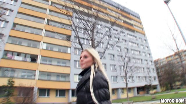 Blonde Mia Angel in leather jacket walks by apartments outdoors