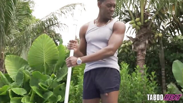 Muscular black man in tank top and shorts with pole, tropical vibe