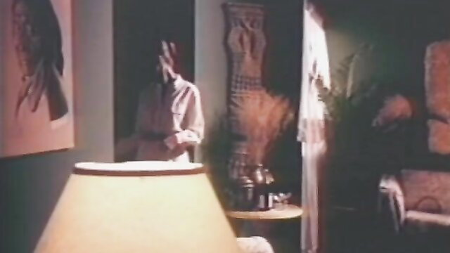 Peaches A in white robe, seductive pose in classic VHS bedroom scene