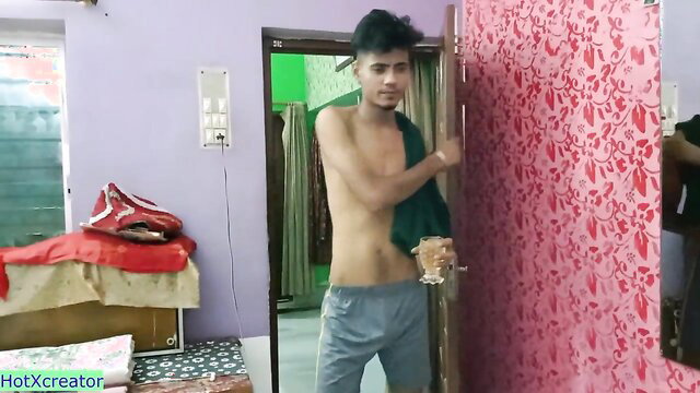 Slim shirtless Indian twink in grey track pants holding drink in bedroom