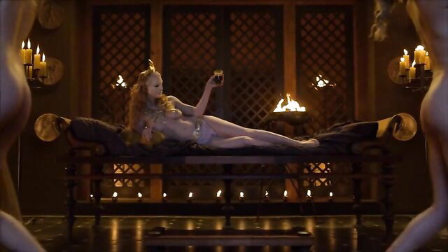 Blonde beauty in gold bikini lounges seductively on bed in erotic Roman scene