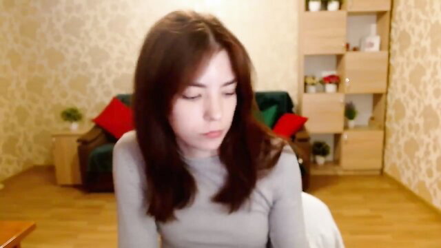 Brunette amateur babe in gray sweater holding blue toy on webcam tease