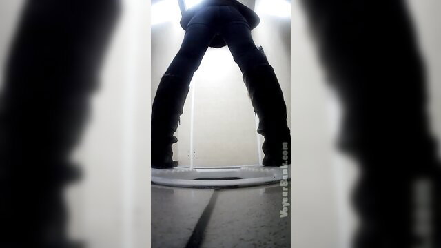 Curvy white chick in tight pants and boots stands over toilet in public restroom