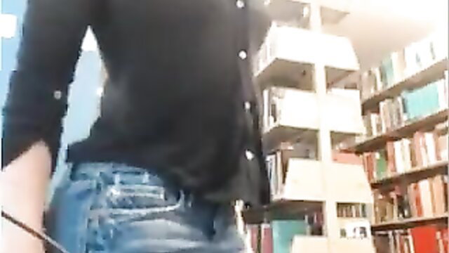 Nerdy girl in black blouse and tight jeans poses sexy in library