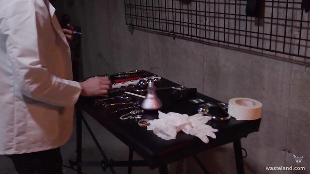 Scientist in lab coat preps BDSM tools for bound humiliation kinky fun