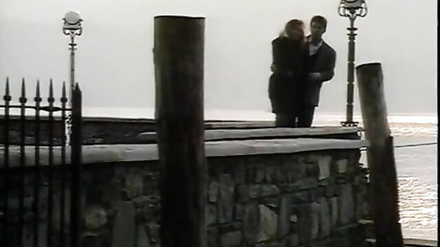 Retro couple in trench coats embracing on foggy pier, classic tease