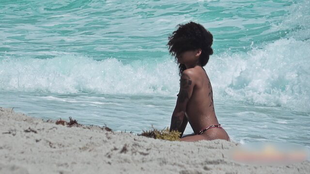 Curvy black babe with tattoos sits nude on beach in voyeur video