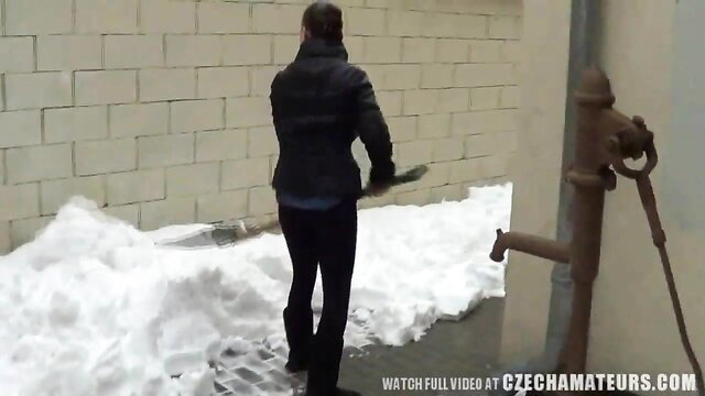 Hot brunette in tight pants and boots shoveling snow outdoors