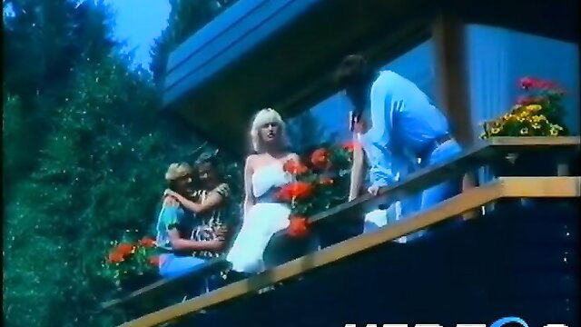 Retro blonde babe in white dress hugged by men on balcony