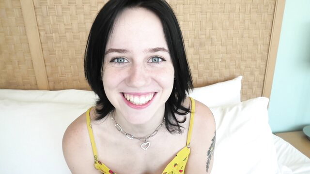Smiling black-haired teen in yellow top smiles at camera on bed