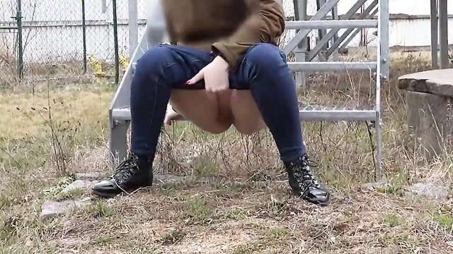 Slim brunette woman squatting outdoors pulling down tight jeans to piss