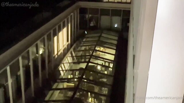 Jade in dimly lit glass atrium corridor at night, adult tease